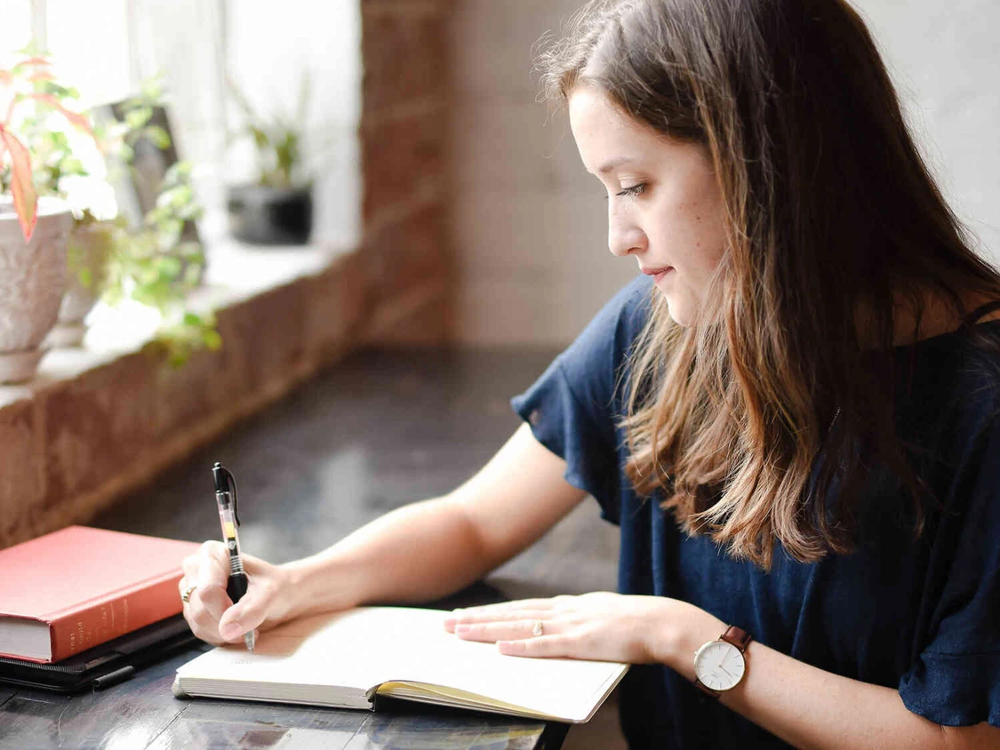 Frau sitzt an einem Tisch und macht notizen in ihr notiz buch