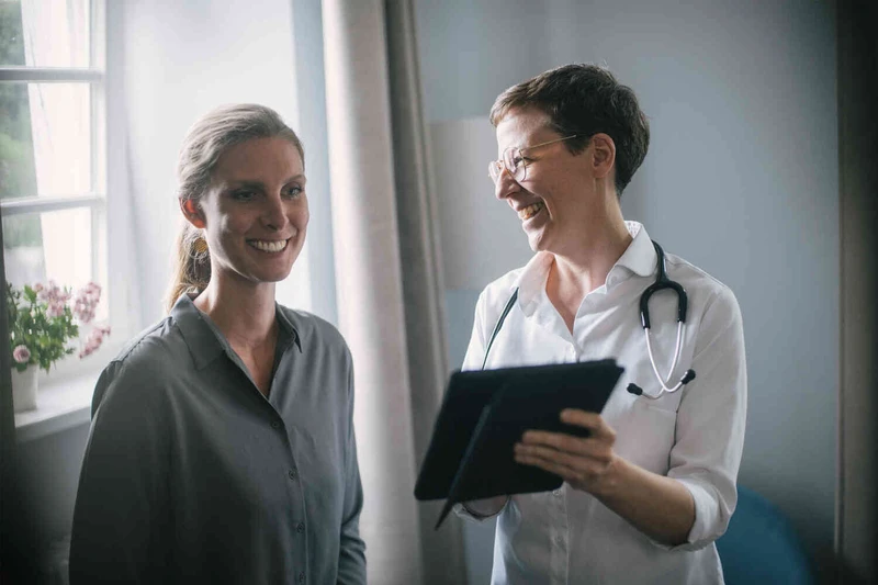 &Auml;rztin im Gespr&auml;ch mit Patientin, beide l&auml;cheln